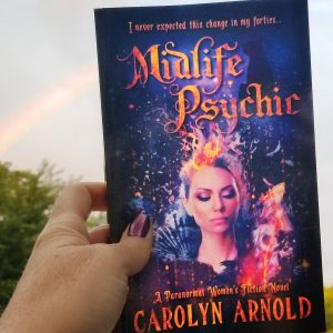 Midlife Psychic by Carolyn Arnold in her hand with a rainbow in the sky